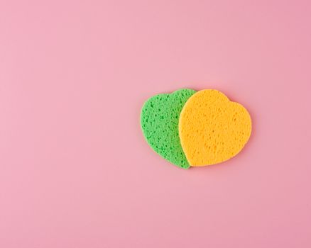 green and yellow heart shaped sponge for face wash on pink background, top view