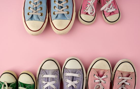 many multi-colored well-worn textile sneakers of different sizes on a pink background, top view, concept, family and team, friendship, copy space