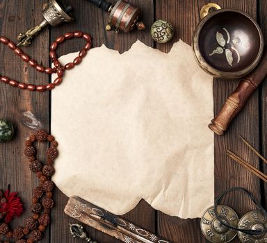 tibetan religious objects for meditation and alternative medicine, empty crumpled brown sheet of paper on a brown wooden background, top view