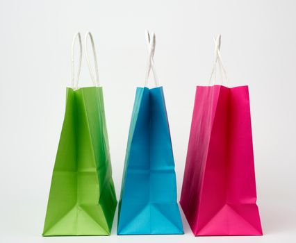 empty multicolored paper bags for shopping and gifts with white handles stand on a white background, copy space