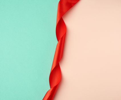 twisted silk red ribbon on a green-beige background, top view