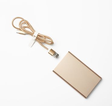 golden power bank and cord with a usb connector for recharging mobile devices on a white background, top view