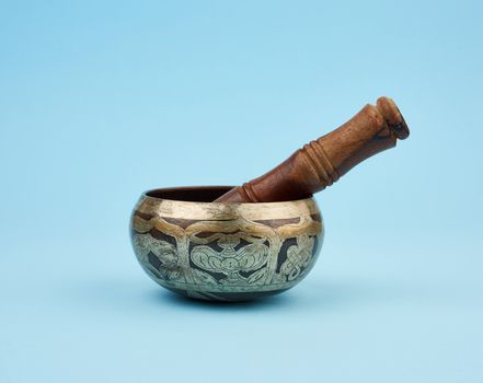 copper singing bowl and wooden stick on a blue background, a Tibetan musical instrument for meditation and alternative medicine