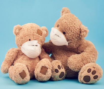 big brown teddy bears are sitting in medical masks on a blue background, concept of protection from respiratory disease, virus and individual respiratory protection