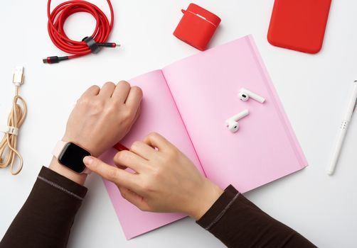 smart watch with a blank black screen is on his left hand, his right hand is touching the watch screen, a freelancer’s workplace with an open notebook, top view, work at home