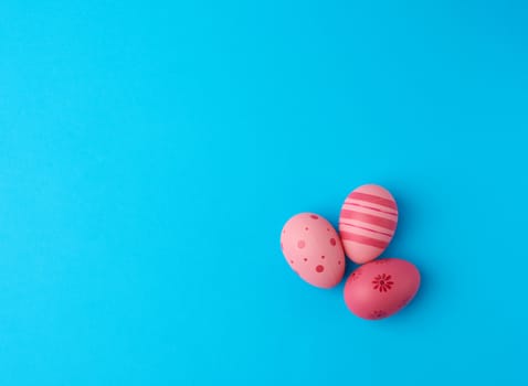 three colored pink easter eggs on a blue background, close up, copy space