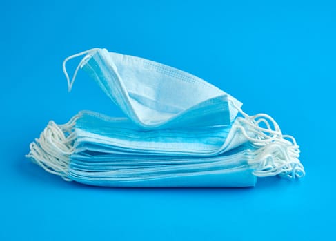 stack of medical masks made of non-woven material with white rubber bands on a blue background, protective accessory for the respiratory tract from the virus, top view