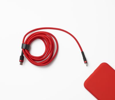 red smartphone and cable in textile braid on a white background, close up, flat lay