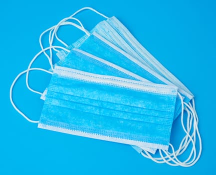 stack of medical masks made of non-woven material with white rubber bands on a blue background, protective accessory for the respiratory tract from the virus, top view