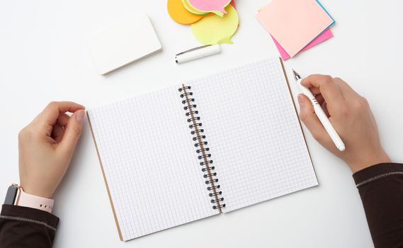 open notebook and two female hands with pen, top view, workplace