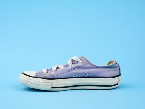 purple worn textile sneaker with white laces on a light blue background, side view of shoes