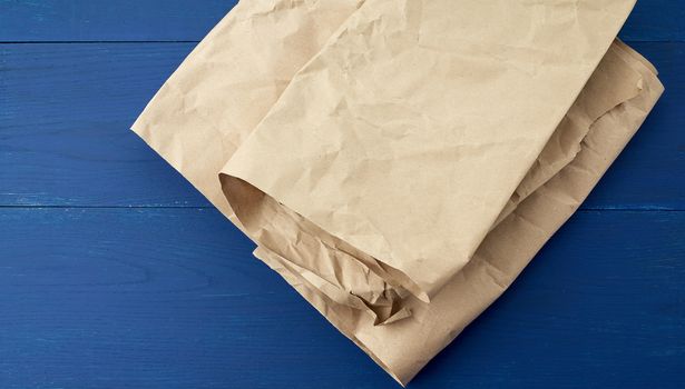 folded brown crumpled kraft paper sheet on blue wooden background, close up