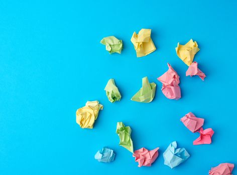 crumpled multi-colored paper stickers, top view, blue background