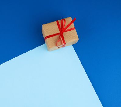 box wrapped in brown paper and tied with a red bow, gift on a blue background. Great design for any purposes. Holiday background. Valentine gift.