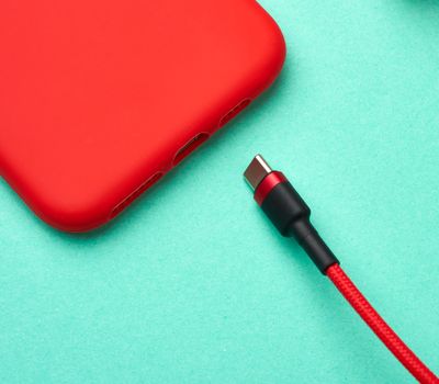 red smartphone and cable in textile braid on a green background, close up