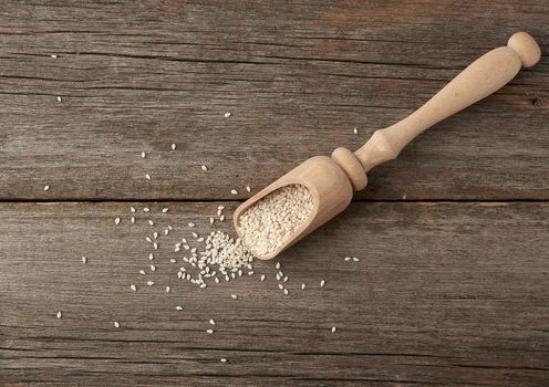 dry white sesame seeds in a brown wooden spoon on a gray wooden table from old boards, top view