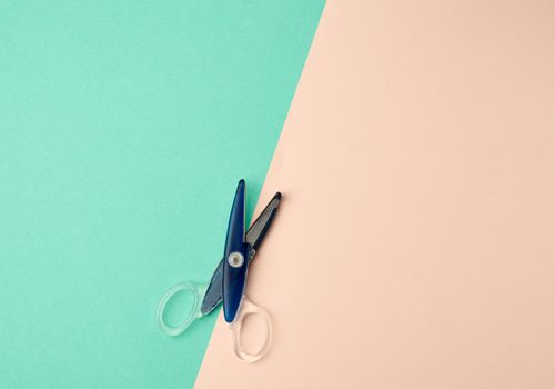 blue plastic paper scissors on a green-beige background, top view, flat lay