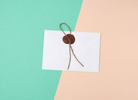 rectangular white paper envelope and brown stamp, color background, flat lay