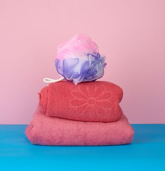 stack of pink folded towels and a plastic washcloth on a blue background, bath set