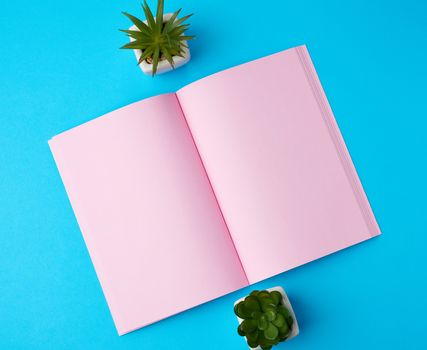open notebook with blank pink pages on a blue background, top view, flat lay