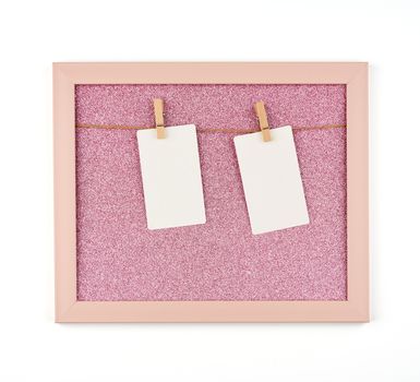 pink shiny frame with ropes and empty white paper sheets hanging on wooden clothespins, place for photo and inscription