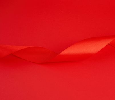 twisted red silk shiny ribbon on a red background, festive design element, close up