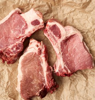 raw juicy pork slices of meat on the rib, food lies on brown parchment paper, top view
