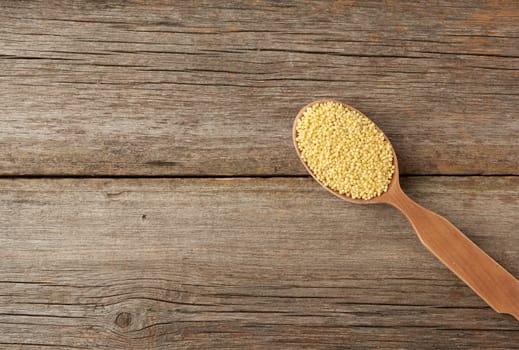 yellow millet cereals in a wooden spoon on a gray wooden table, top view, copy space