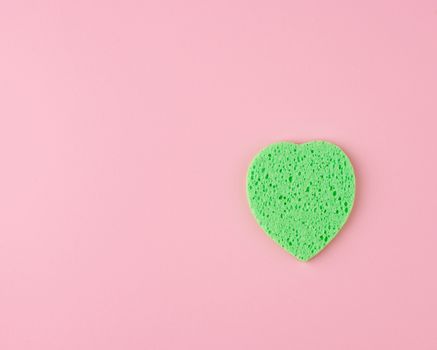 green heart shaped sponge for face wash on pink background, copy space
