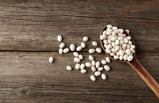 white raw whole beans in a brown wooden spoon on the table, top view