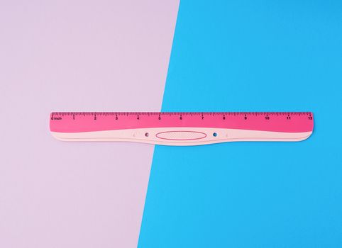pink plastic ruler on a colored background, top view, flat lay