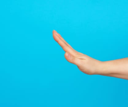 hand shows stop gesture on a blue background, close up