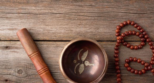 Tibetan singing copper bowl with a wooden clapper and prayer rosary on a gray wooden table, close up