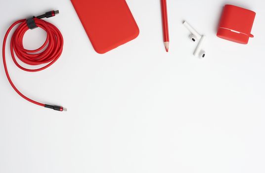 red smartphone, wireless headphones and cable in textile braid on a white table, top view, flat lay