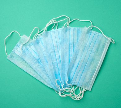 stack of disposable blue medical masks on a green background, top view