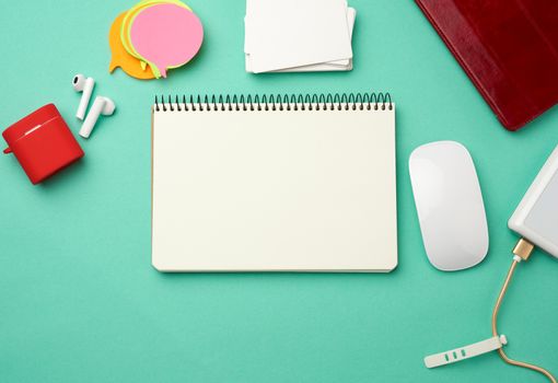 open notebook with blank white sheets, computer mouse, wireless headphones and charger, top view