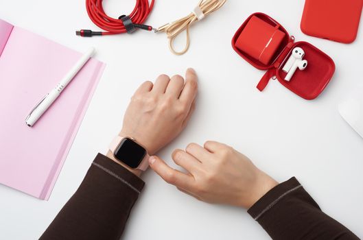 smart watch with a blank black screen is on his left hand, his right hand is touching the watch screen, freelancer’s workplace with an open notebook, top view, work at home