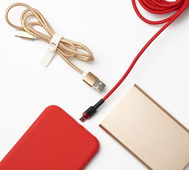 golden power bank, red smartphone and cable in textile braid on a white background, close up, flat lay
