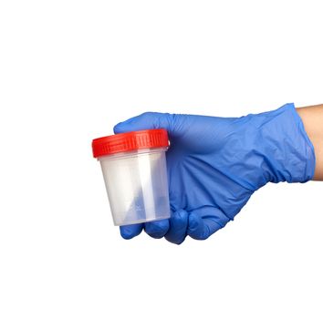hand holds a transparent plastic jar with a red lid for urine tests, part of the body is dressed in blue medical sterile gloves and isolated on a white background