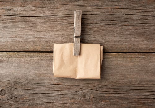 wooden clothespin and folded brown paper on a gray wooden background, close up