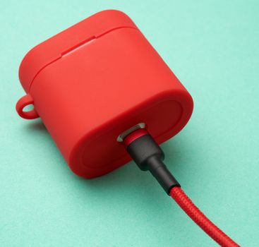 box with a headphone charger in a red case attached to the cable on a green background, close up