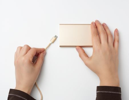hands holding a portable power bank and a golden cable on a white background, top view