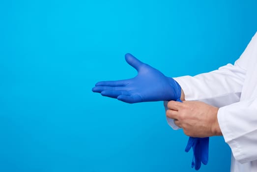 male doctor in white uniform puts on his hands blue sterile latex gloves before surgery, white background, copy space