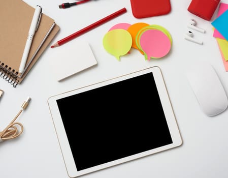 freelancer workplace at home, electronic tablet with blank black screen, multi-colored paper stickers, smartphone and wireless headphones, white table, top view