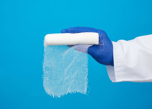 male hand in blue sterile gloves holds a white twisted gauze medical bandage on a blue background, treatment of injuries