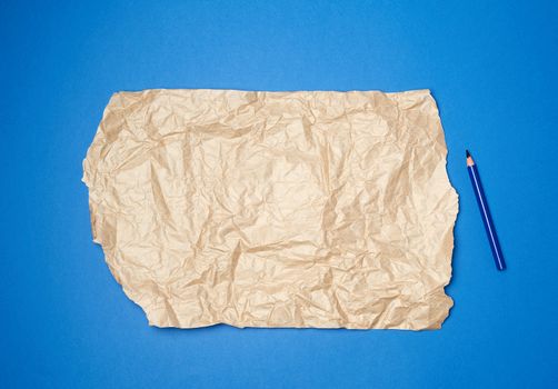 sheet of brown crumpled paper for packaging on a dark blue background and wooden pencil, close up