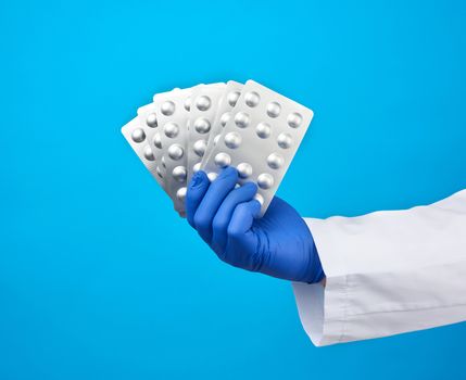 male hand with blue sterile gloves holds a pills in a blister, concept for drug treatment of diseases, blue background