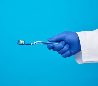 doctor therapist is dressed in a white robe uniform and blue sterile gloves holding a toothbrush, daily brushing concept, blue background