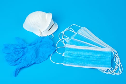 disposable gloves and stack of medical masks made of non-woven material with white rubber bands on a blue background, protective accessory for the respiratory tract from the virus, set