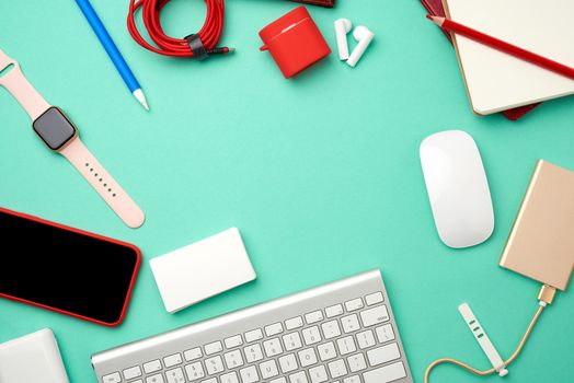 keyboard, golden power bank with cable, red smartphone with blank black screen, headphones, blank paper business cards and wireless mouse on green background, workplace, top view